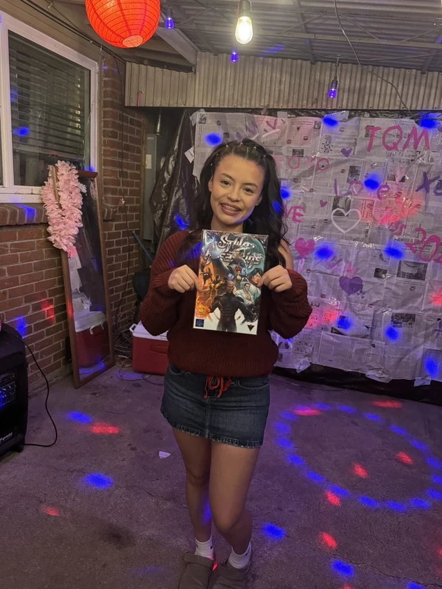 Reader holding the Style Assassins standard-cover comic beneath colored lights.