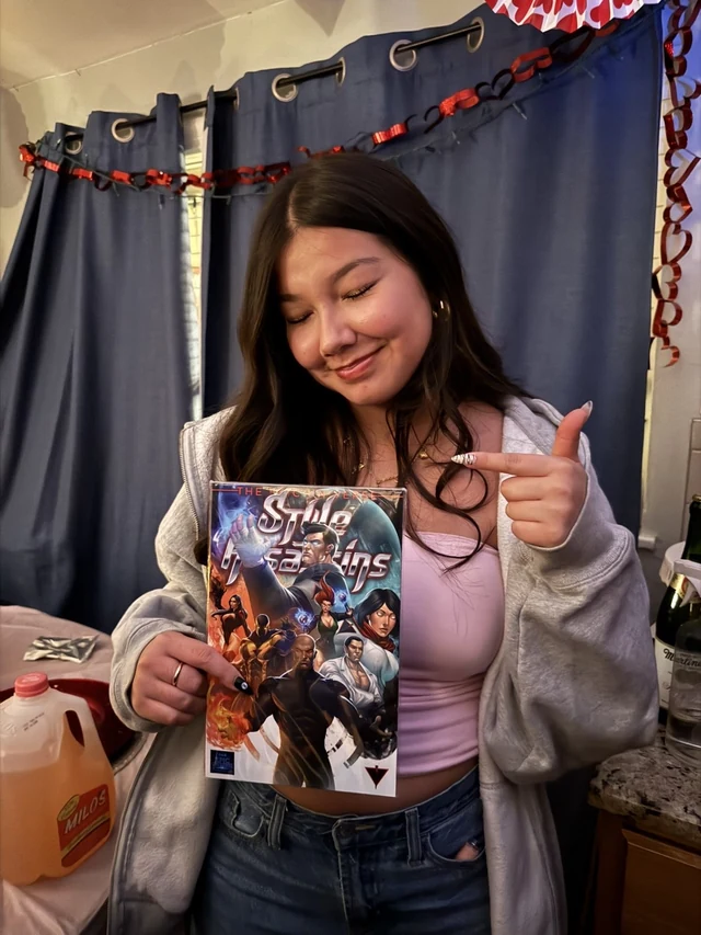 Reader holding the Style Assassins standard-cover comic and pointing toward its cover.